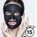 A woman wearing a black charcoal face mask, with her hands framing her face against a light gray background. A black stopwatch icon with the number 15 is in the bottom right corner. Garnier AHA + BHA Charcoal Mattifying Serum Sheet Mask Oily Skin