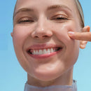 Close-up of a smiling woman's face with a finger touching her cheek, set against a solid light blue background. Garnier Hyaluron+ Barrier Repair Serum Mask 1 Pack