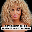 Woman with blonde curly hair against a black background with text about hair care. Garnier Olia Hair Colour Max Bleach Blonde