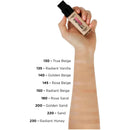 Hand holding a foundation bottle with color swatches on a white background