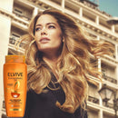 Woman with flowing blonde hair holding a bottle of L'Oreal Elvive shampoo against an urban background