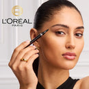 A close-up of a woman holding an eyebrow pencil near her brow, with the L'Oréal Paris logo visible in the upper left. The product appears to be an eyebrow pencil, shown being used on a model.