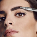 Close-up of a woman's face with a silver L'Oréal Paris Micro Unbeliever eyebrow pencil being applied to her eyebrow. buy L'Oreal Paris Infallible Brows 48H Micro Tatouage Ink Pen 3.0 Brunette