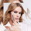 A close-up beauty shot of a woman with blonde hair holding a makeup pencil near her face, wearing a white collared shirt against a clean white background. L'Oreal Paris Paradise Le Khol Eyeliner 101 Midnight Black