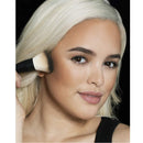 Woman applying makeup with a brush on a plain background