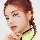 A close-up of a woman with reddish-brown braided hair holding a black eyeliner pen, wearing a bright neon yellow top against a clean light gray background.