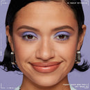 Close-up beauty shot of a woman with purple eyeshadow and nude lip color, wearing silver hoop earrings against a lavender background. Text at the top reads 'NO MAKEUP RETOUCHING' and text at the bottom reads 'POWDER LOUDER BROW PENCIL SOFT BROWN 62'. NYX Powder Louder Eyebrow Pencil 05 Soft Brown
